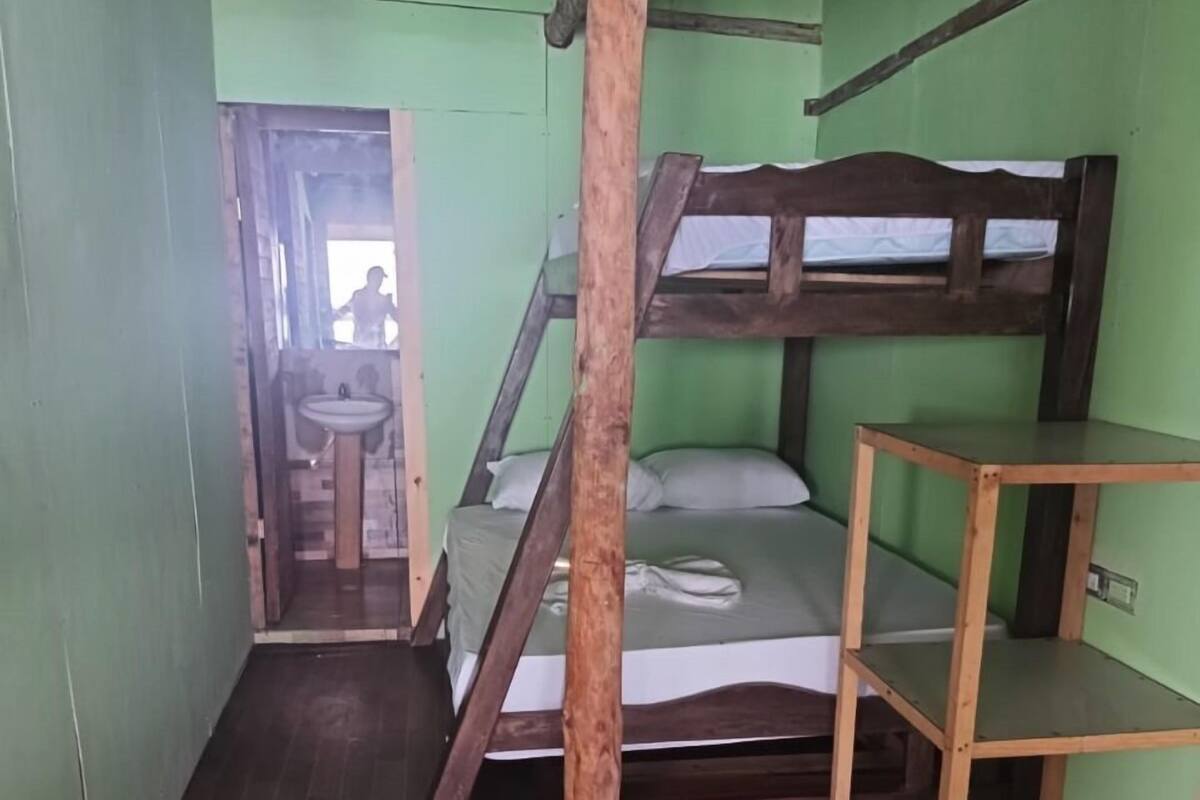 A bunk bed room with a wooden ladder, a small wooden shelf, and a bathroom visible through an open door.