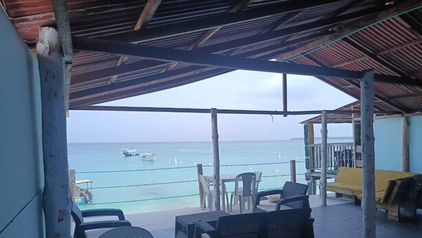 A covered outdoor seating area with wicker furniture and a view of the sea.