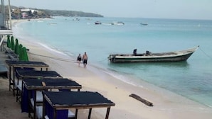 A beach with rows of blue plastic chairs and tables, a boat in the water, and a sandy shore.