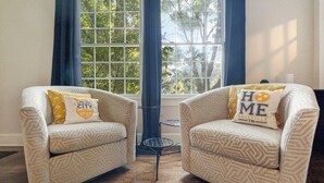 Dos sillones con tapicería estampada, una mesita metálica pequeña y una ventana con cortinas azules.