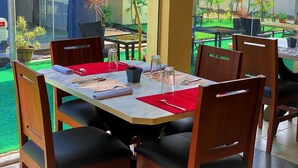 A dining area with a table set for four, surrounded by chairs, and a view of a garden with various plants. - Klulead Garden and Suites (Ijebu Ode)