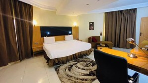 A hotel room with a large bed, a desk with a chair, a sofa, and a TV. - Klulead Garden and Suites (Ijebu Ode)