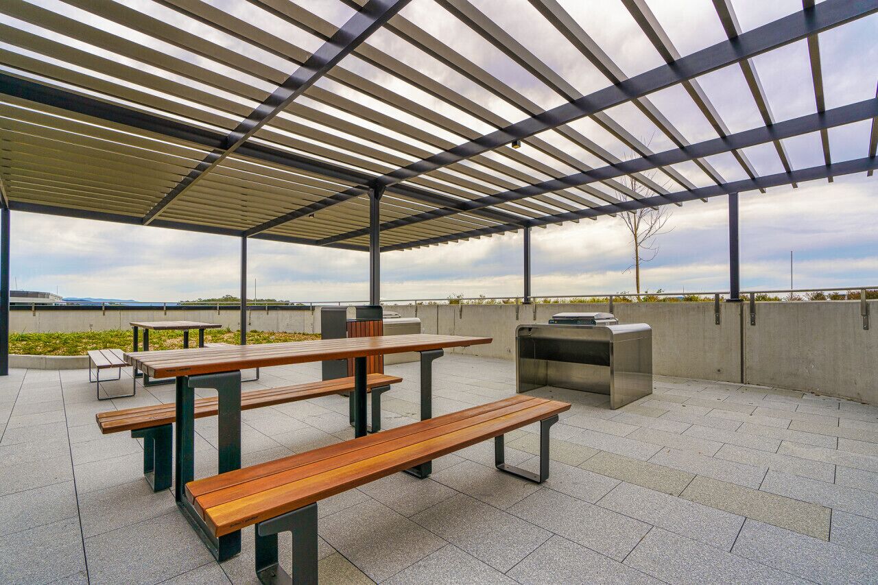 Ein Außenbereich mit einer Terrasse, Picknicktischen und einem Grill.