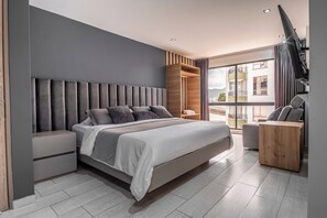 A modern bedroom with a large bed, a nightstand, a wooden wardrobe, and a TV. - Hotel Plaza doce (Pereira)