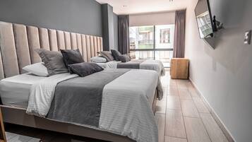 Ein modernes Hotelzimmer mit einem großen Bett, einem kleineren Bett und einem Holfnachtkästchen.