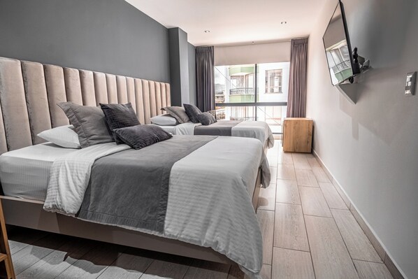 A modern hotel room with a large bed, a smaller bed, and a wooden nightstand. - Hotel Plaza doce (Pereira)