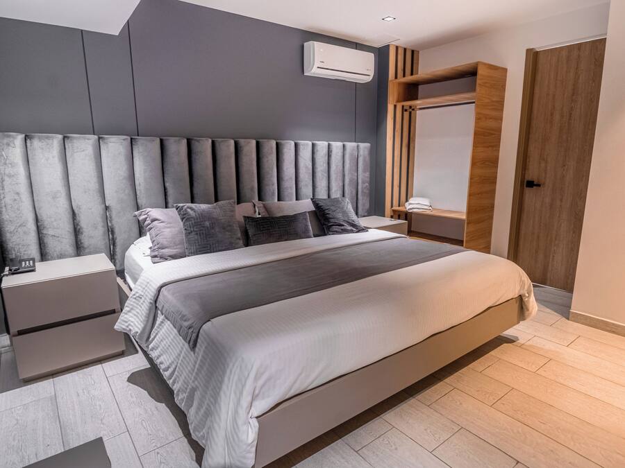 Un dormitorio moderno con una cama grande, cabecero tapizado en gris, mesitas de noche y un armario empotrado.
