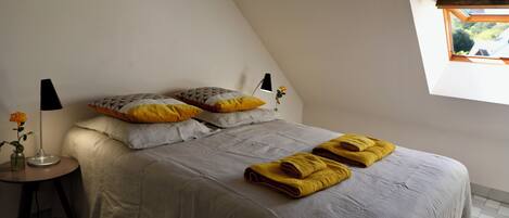 Een slaapkamer met een bed, kussens, een nachtkastje met lamp en een raam met uitzicht.