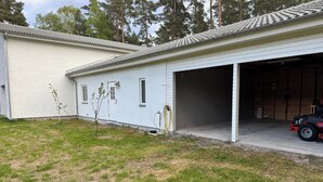 A building with a garage and a small tree in front. - In the Middle of the Forest Nearby Ahus (Aahus)