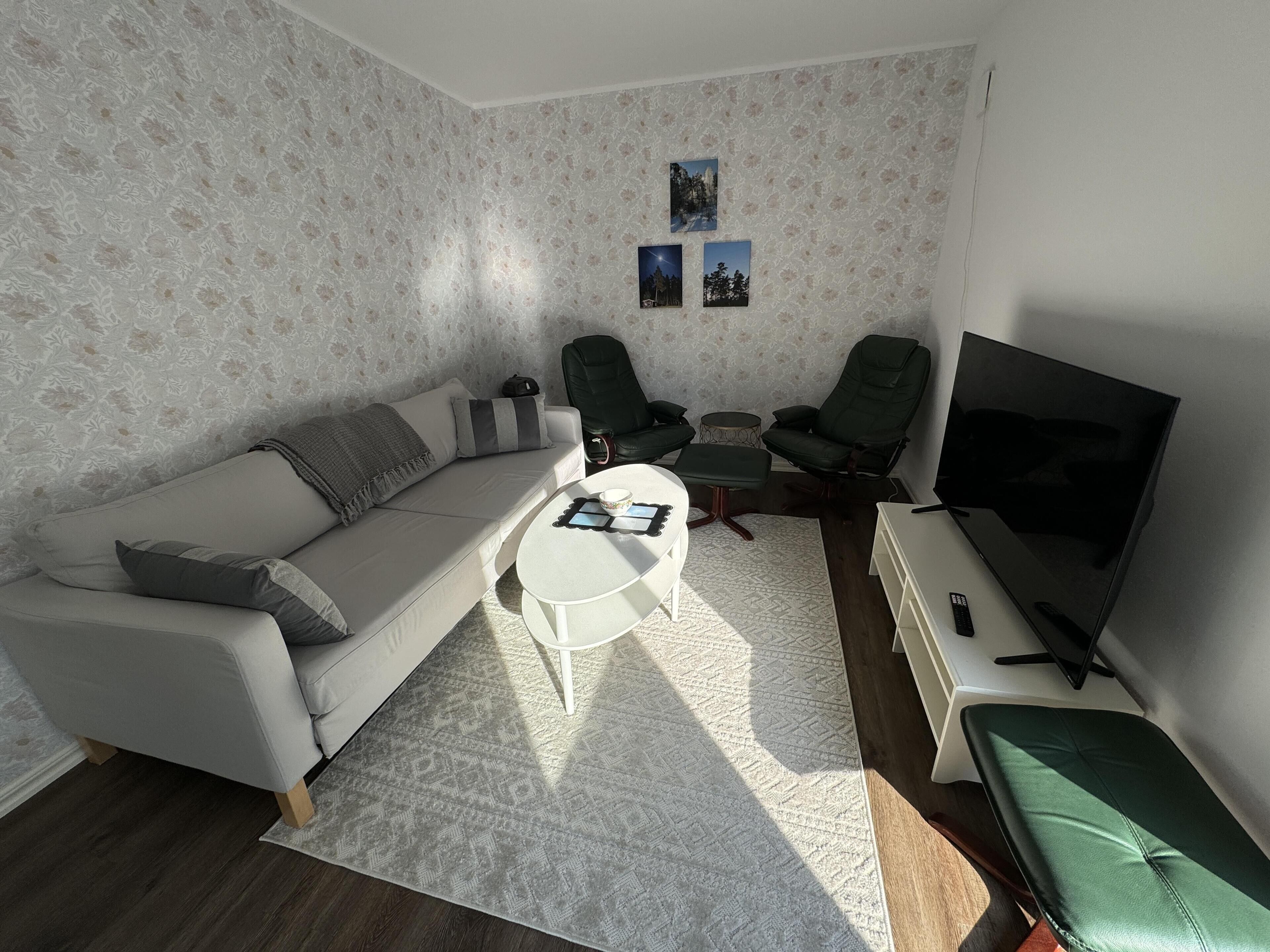 A living room with a sofa, two armchairs, a coffee table, a TV, and a small rug.