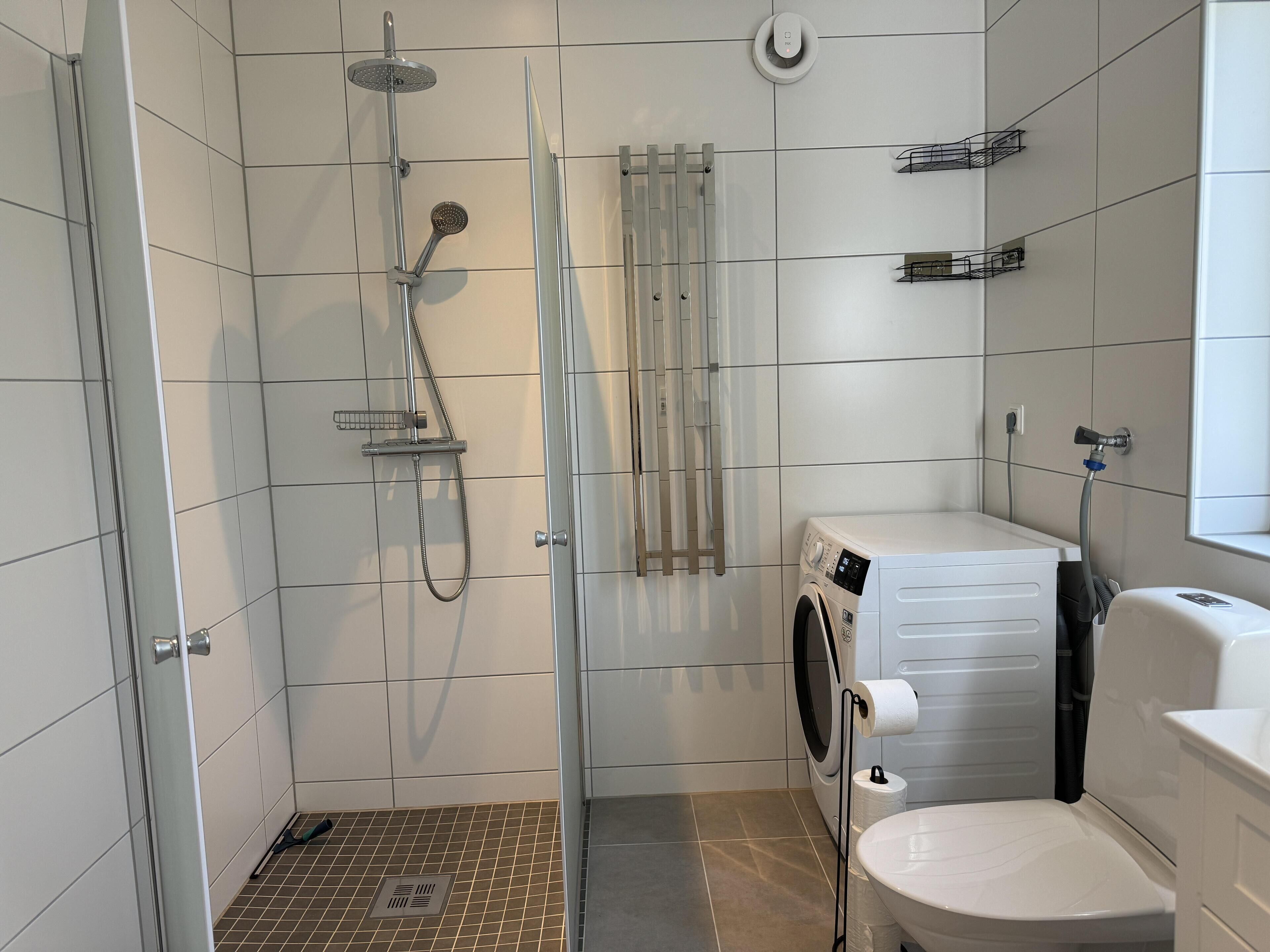 Un baño moderno con ducha de vidrio, lavadora integrada y un inodoro.