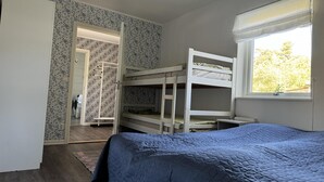 Ένα υπνοδωμάτιο με κουκέτες, ένα παράθυρο με θέα σε δέντρα και μια πόρτα που οδηγεί σε ένα άλλο δωμάτιο.