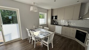 A modern kitchen with white cabinets, a herringbone backsplash, and a dining area with a white table and chairs. - In the Middle of the Forest Nearby Ahus (Aahus)