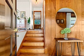 A wooden staircase leading to a kitchen area with a round mirror and a small table with a plant.