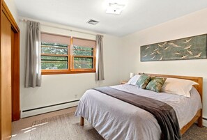 A bedroom with a bed, curtains, a window, and a wall art piece.