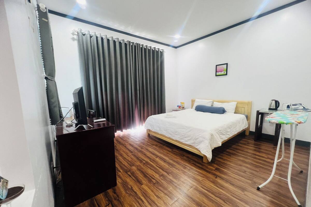 A hotel room with a bed, a desk, a chair, a TV, and a curtain.