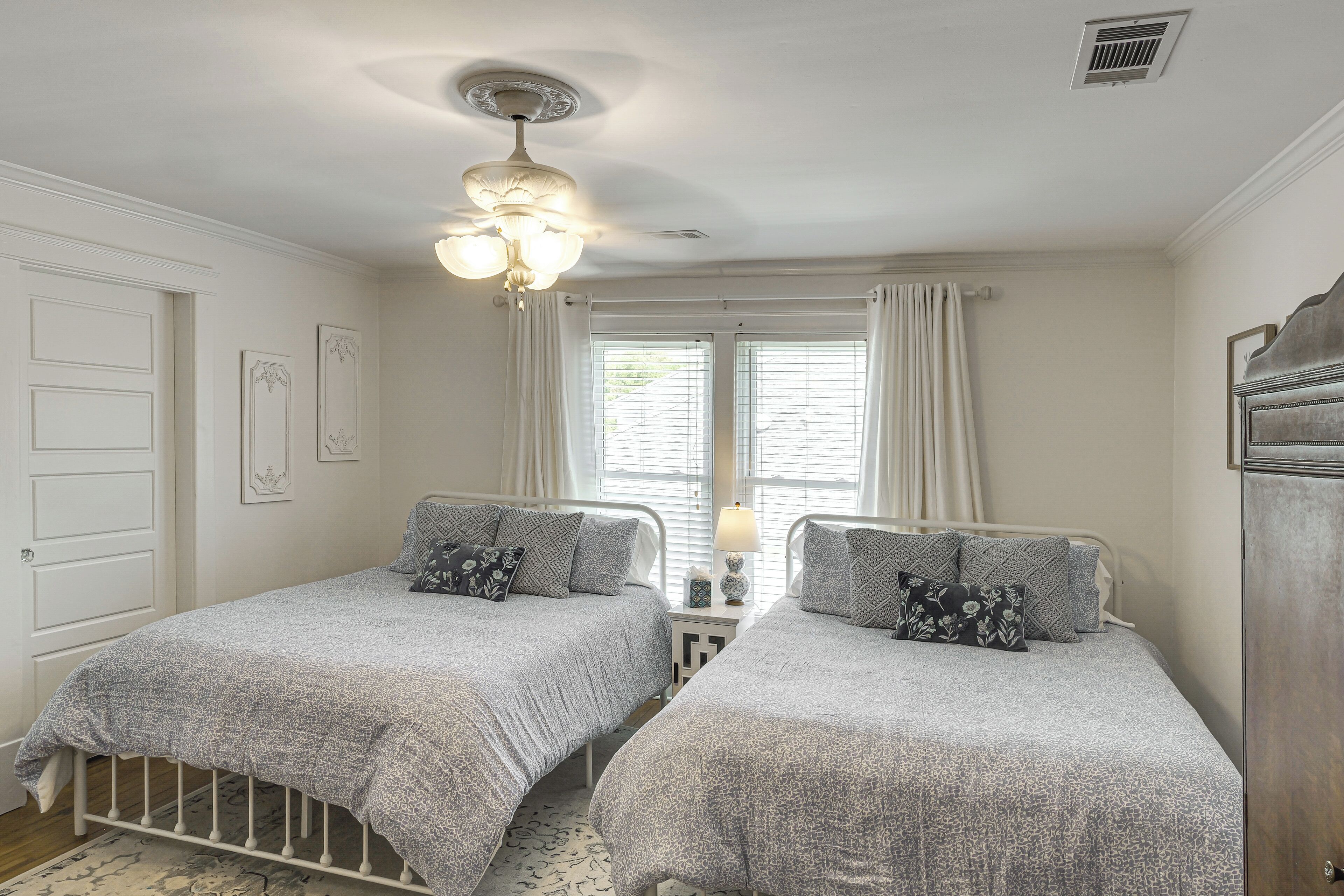 A bedroom with two single beds, a ceiling fan, a window with curtains, and a door.