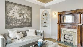 A living room with a grey sofa, a fireplace, and a large floral painting.