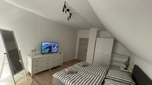 Un dormitorio con cama, televisor, armario y espejo.
