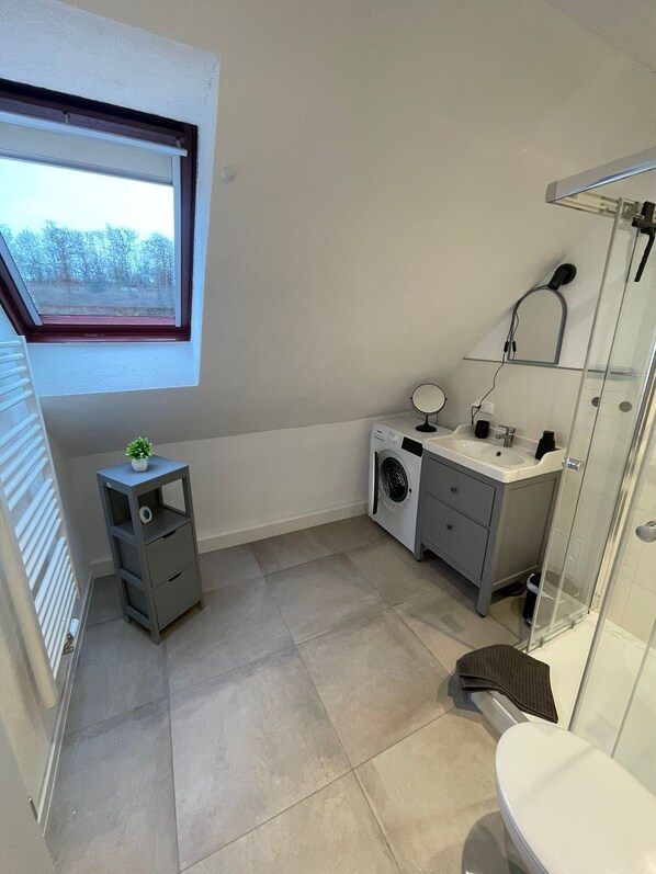 Un baño pequeño con ventana, lavadora, lavabo e inodoro.