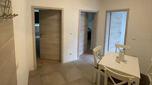 Una habitación con una mesa de comedor y sillas, una puerta que da a otra estancia, y una lámpara en el techo.