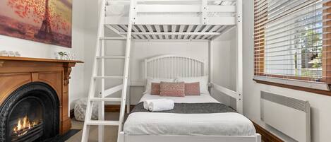 Een stapelbed met een ladder, een open haard en een raam met zonwering.