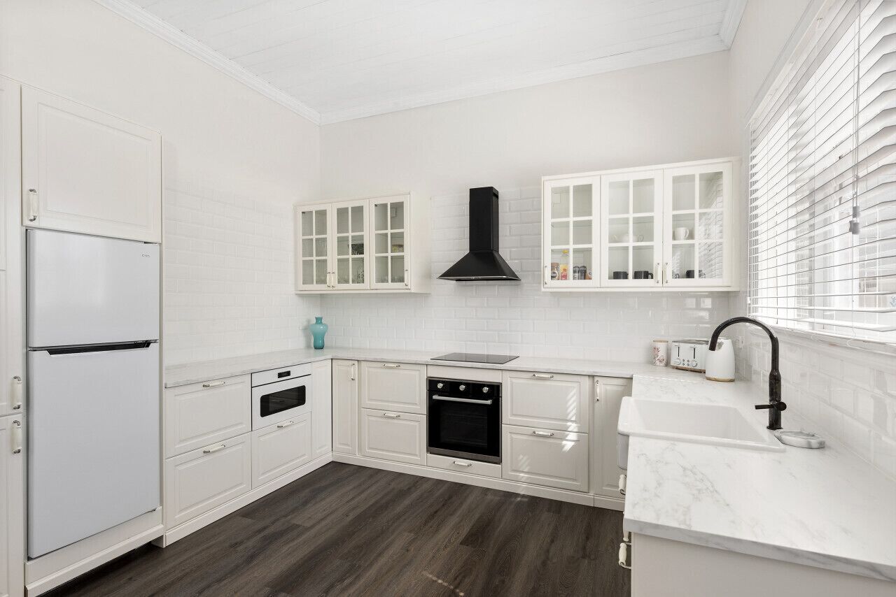 A kitchen with white cabinetry, a black range hood, a built-in oven, a microwave, and a sink with a faucet.