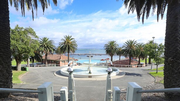 A view of a fountain surrounded by palm trees and a body of water.