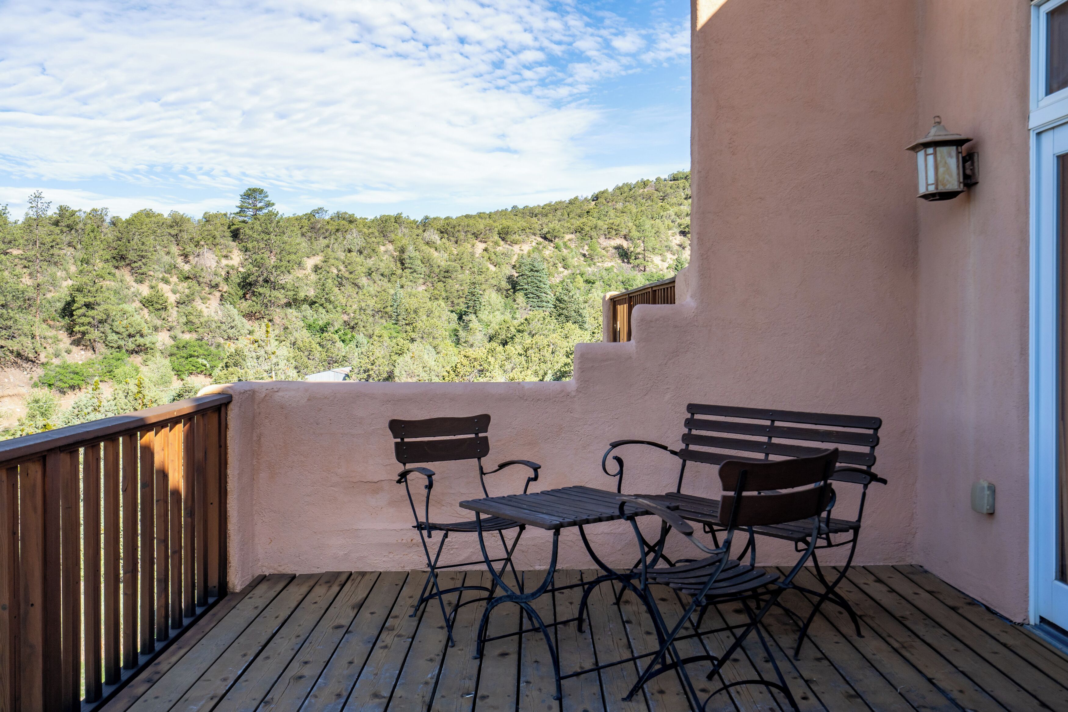 A balcony with a wooden deck, two metal chairs, and a small table.