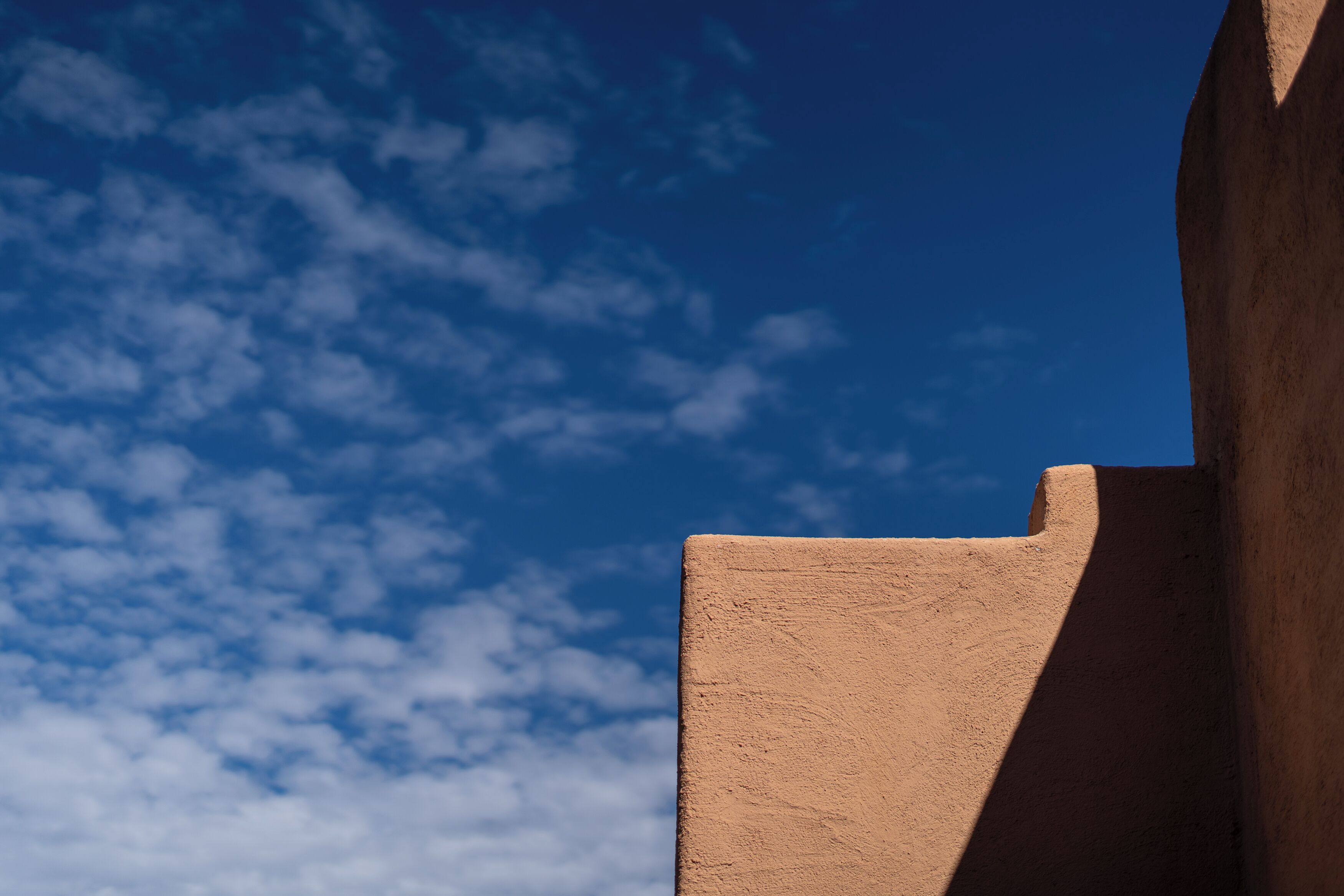 A building corner with a clear blue sky and scattered clouds.