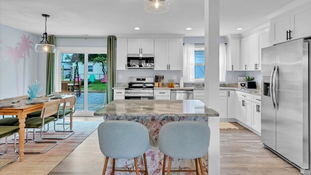 A modern kitchen with white cabinets, stainless steel appliances, and a large island with bar stools. - Charming 3bd - Near beaches - Foosball & Backyard (Norfolk)