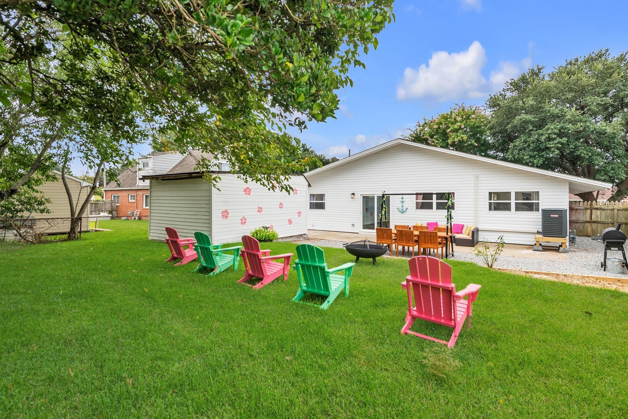 Un jardin avec une maison blanche, une pelouse verte et des fauteuils Adirondack rouges et verts.
