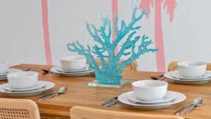 A dining table set with white bowls and plates, a blue coral centerpiece, and a wall with a palm tree mural. - Charming 3bd - Near beaches - Foosball & Backyard (Norfolk)