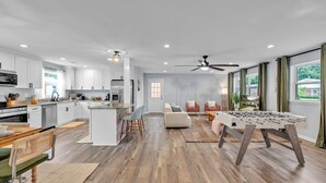 A modern kitchen with white cabinets, a central island, and a dining area with a wooden table and chairs. - Charming 3bd - Near beaches - Foosball & Backyard (Norfolk)
