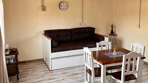 A cozy room with a wooden ceiling, a brown leather sofa, a white table with chairs, and a wall clock. - Departamento cerca del centro (El Calafate)