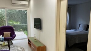 Een moderne slaapkamer met een bed, een aan de muur bevestigde televisie en een klein houten nachtkastje.