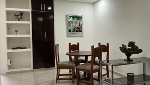 Een eetgedeelte met een ronde tafel en vier stoelen, een donker kastmeubel en een glazen tafel met een decoratief object.