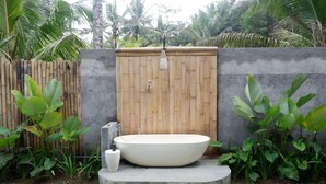 A freestanding bathtub in a garden setting with a wooden fence and tropical plants. - Pitu A Punggul Village Escape (Abiansemal)