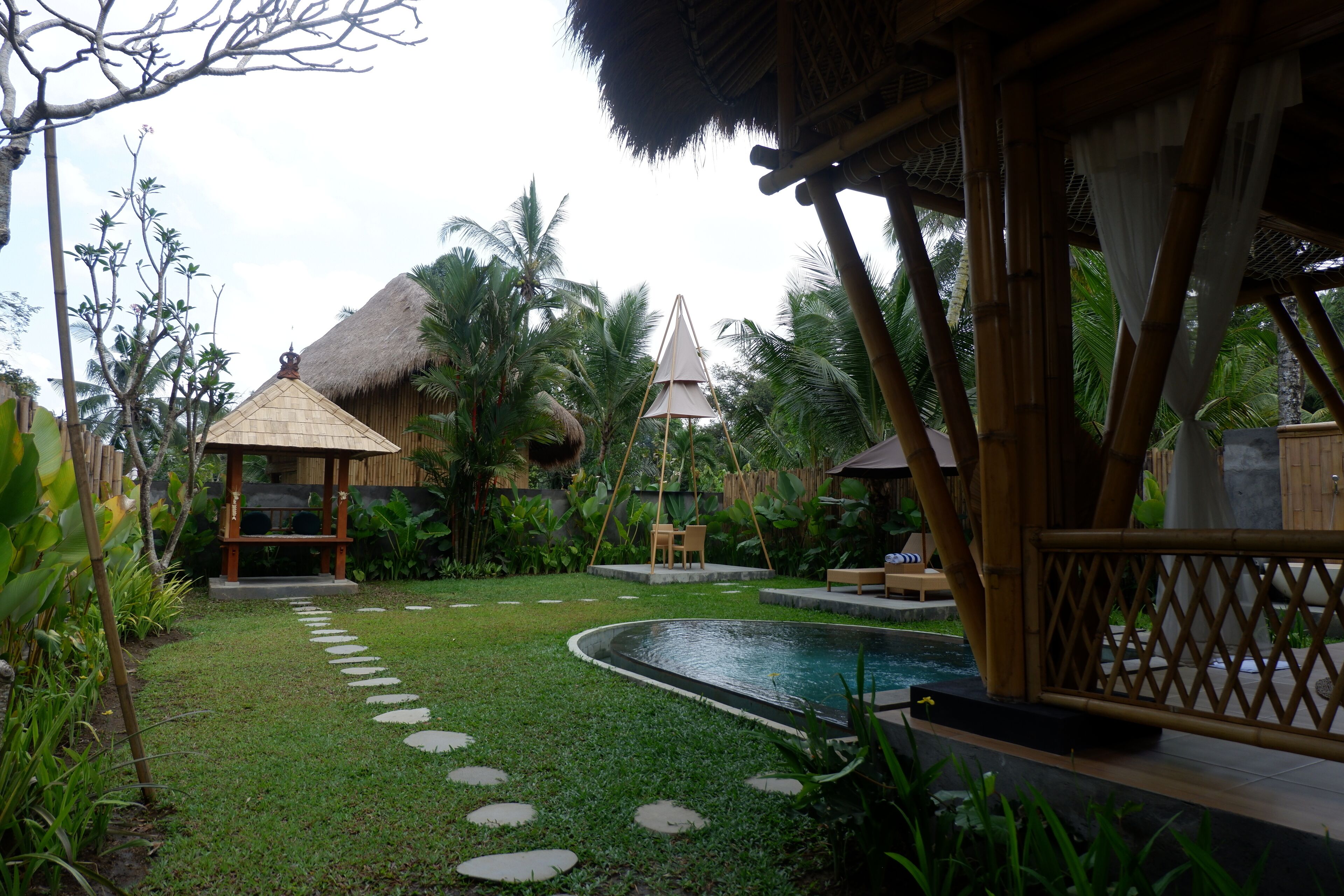 A pool area with a thatched-roof structure, a swing chair, and a bamboo fence.