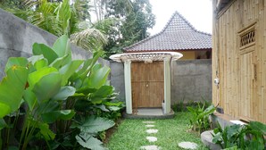 A garden with a wooden door, a concrete wall, and a tiled roof structure. - Pitu A Punggul Village Escape (Abiansemal)