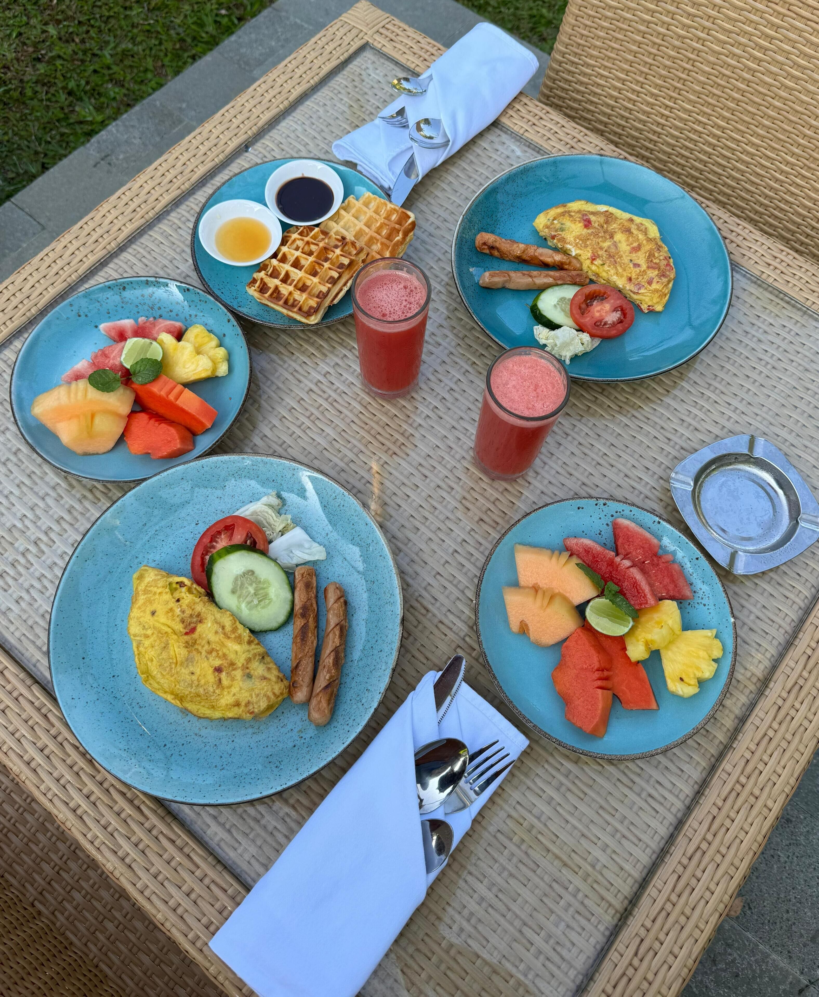A table set with breakfast plates containing waffles, omelets, sausages, and various fruits.