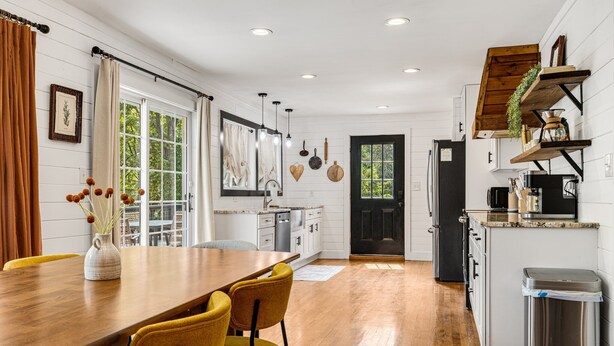 A modern kitchen with white cabinetry, a wooden dining table with yellow chairs, and a black door. - Quiet Furnished 3BR Home Near Asheville - Fast WiFi, Firepit (Canton)
