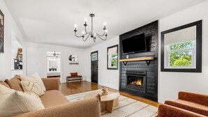 A modern living room with a fireplace, a sofa, and a television mounted on the wall. - Quiet Furnished 3BR Home Near Asheville - Fast WiFi, Firepit (Canton)