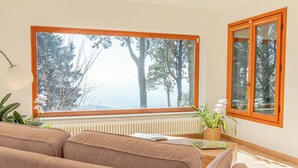 Ein Wohnzimmer mit großem Fenster, Heizkörper, Sofa und einem kleinen Tisch mit Pflanze.