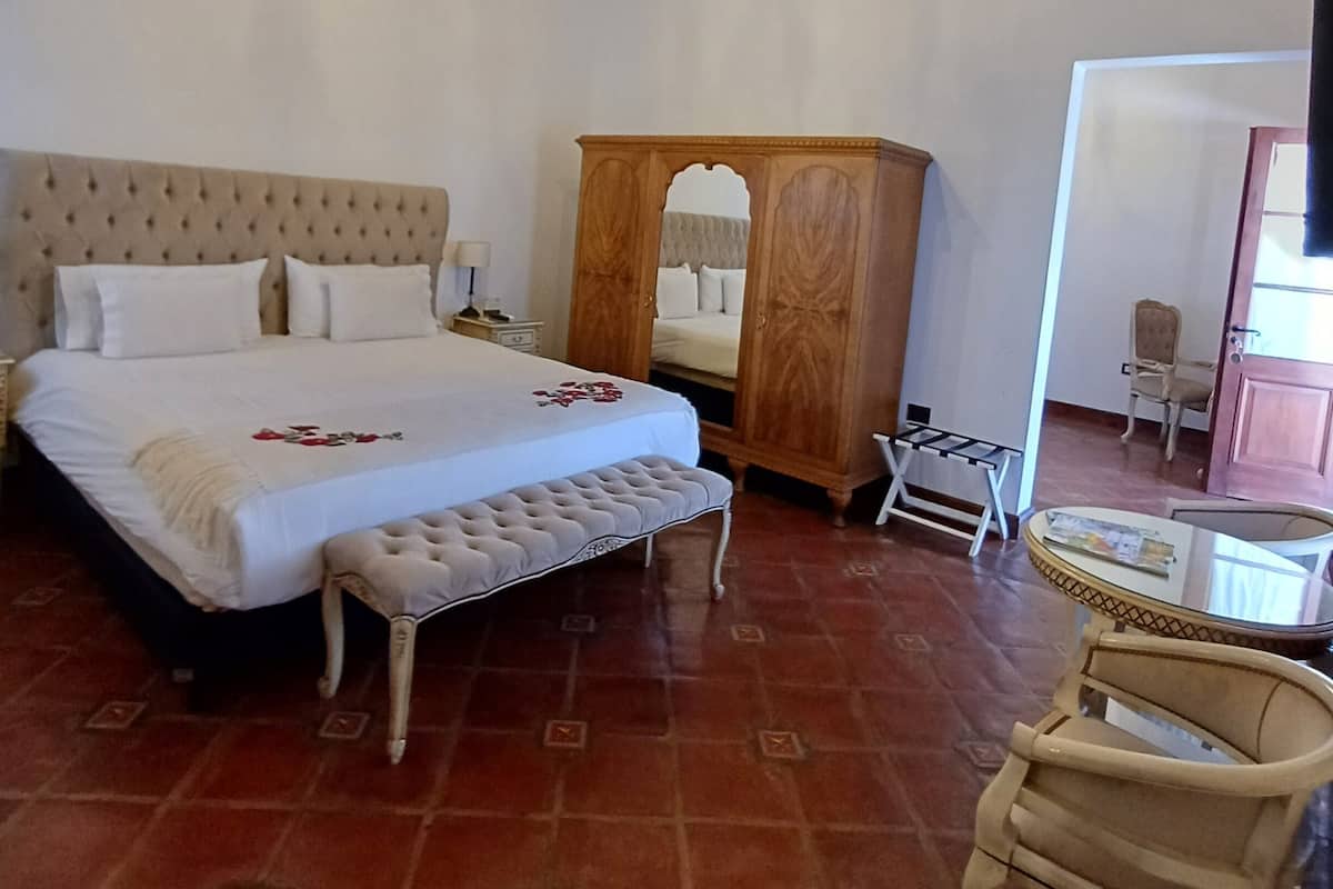 Un dormitorio con una cama grande, un armario de madera, una mesita pequeña y una silla.