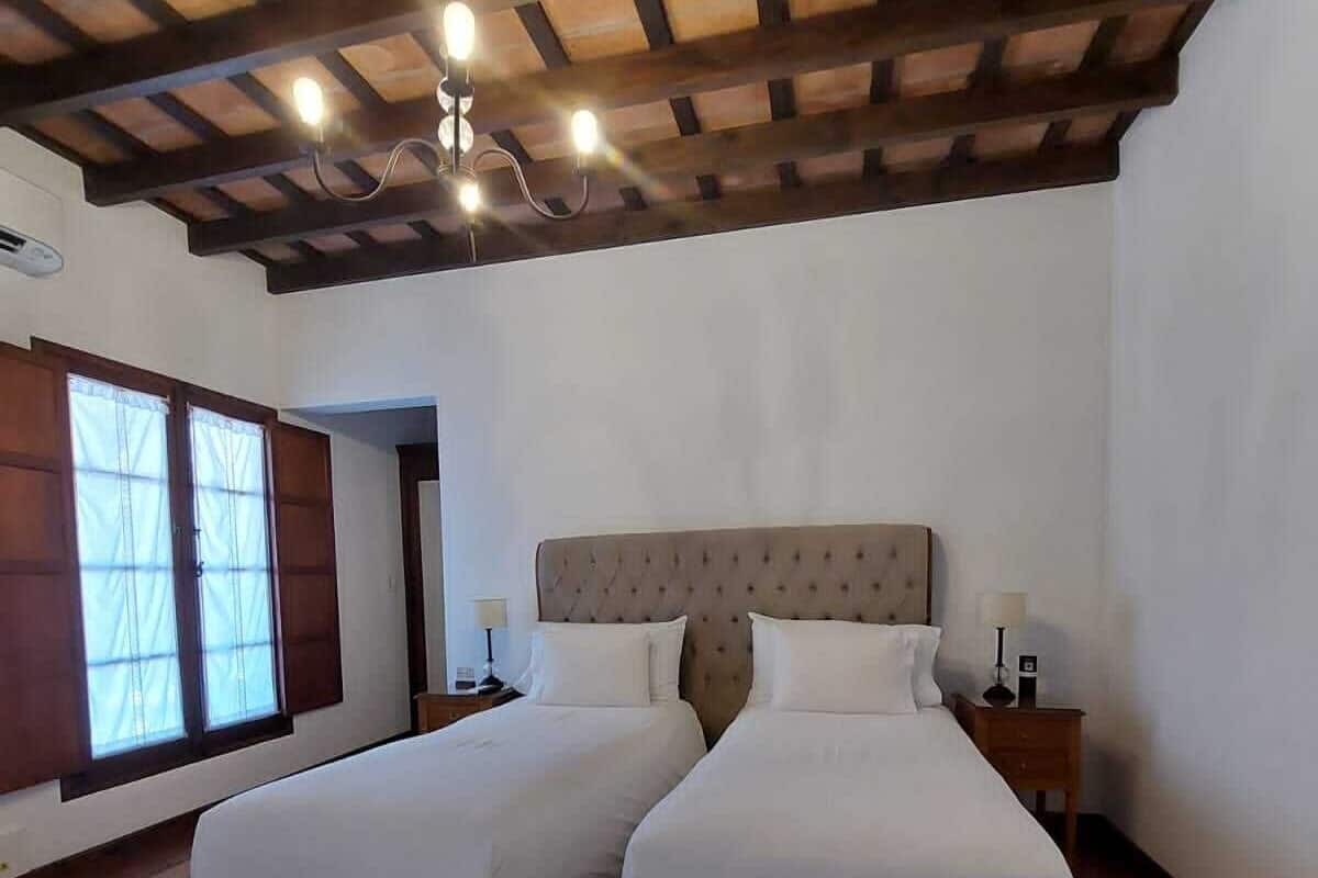Una cama doble con cabecera capitonada, dos mesitas de noche y un ventanal con cortinas.
