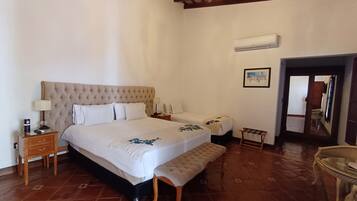 Un dormitorio con una cama grande, dos mesitas de noche, un banco y una araña.