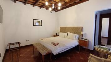 Un dormitorio con una cama grande, cabecera de madera, lámparas de noche, un banco y una pequeña mesa con una silla.