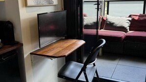 A compact living space with a foldable desk, a flat-screen TV, a sofa, and a sliding glass door leading to an outdoor area. - Little Midnight 1 in the heart of town (Braddon)