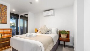 A modern bedroom with a large bed, a bedside table with a plant, and a bookshelf. - Little Midnight 1 in the heart of town (Braddon)